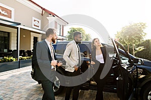 Car salon, sale and rent concept. African and Caucasian men in business wear buying the car. Elegant woman car