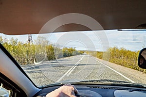 Car salon, steering wheel, hand of woman on it, mirror and view on landscape with road and nature at sunny summer or autumn day.