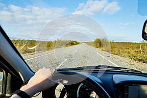 Car salon, steering wheel, hand of woman on it, mirror and view on landscape with road and nature at sunny summer or autumn day.