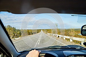 Car salon, steering wheel, hand of woman on it, mirror and view on landscape with road and nature at sunny summer or autumn day.