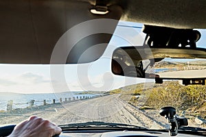 Car salon, steering wheel, hand of woman on it, mirror and view on landscape with road and nature at sunny summer or autumn day.