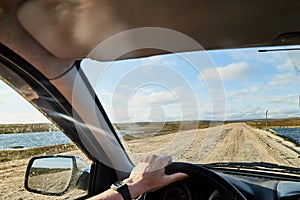 Car salon, steering wheel, hand of woman on it, mirror and view on landscape with road and nature at sunny summer or autumn day.