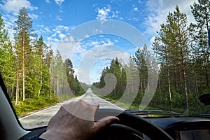 Car salon, steering wheel, hand of woman and view on nature landscape. Road, forest, blue sky, white clouds at sunny day. Concept
