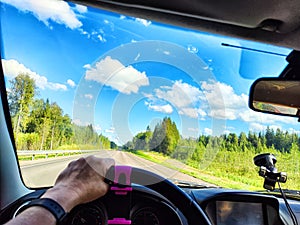 Car salon, steering wheel, hand of woman and view on nature landscape. View from seat of driver on Road, forest, blue