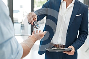 Car Salon. Young man buying car taking keys from agent close-up