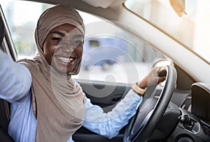 Car Selfie. Cheerful black muslim woman taking self-portrait in her new auto