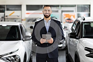 Car seller standing in auto salon and using tablet