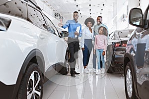 Car selling business. African American family consulting with salesman about purchasing new auto at dealership center