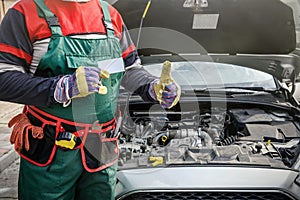 Car service advertising. Mechanic standing near car showing thumb up. Car with opened hood