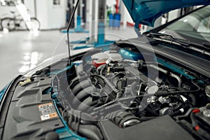 Car service. Close up of a car with open hood under under maintenance in auto repair shop