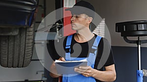 Car service employe inspect car. Mechanic inspects the car undercarriage way and makes a note on his inspection sheet