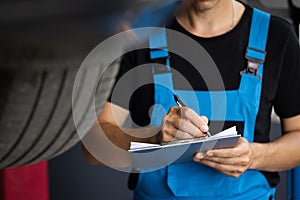 Car service employe inspect car. Mechanic inspects the car undercarriage way and makes a note on his inspection sheet