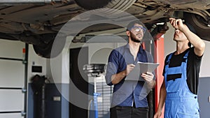 Car Service Employees Inspect the Bottom and Skid Plates of the Car. Manager Checks Data on a Notebook and Explains the