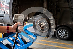 Car service, repair and maintenance concept - auto mechanic man with electric screwdriver changing tire in auto repair shop