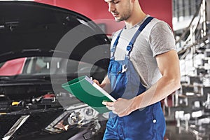 Car service, repair, maintenance and people concept - auto mechanic man or smith with clipboard at workshop