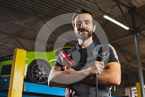 At car service station. One young man, male auto mechanic in dungarees working at car service station, indoors. Concept