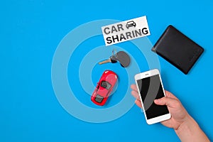 Car sharing app concept. Toy car, car key, auto drive license, human hand with smartphone and text sign