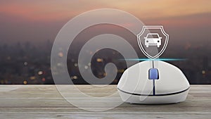 Car with shield flat icon on wireless computer mouse on wooden table over blur of cityscape on warm light sundown, Business automo