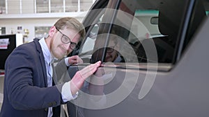 Car showroom, happy purchaser guy spectacles with pleasure stroking new machine gently smiling at Auto sale center