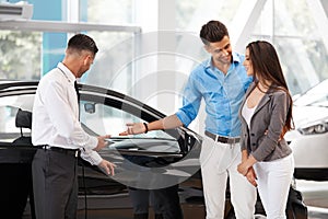 Car Showroom. Young Couple Buying a New Car at Dealership.