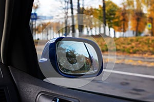 Car side mirror on the background of the autumn road