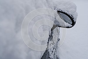 Car side mirror and car window covered with white snow across snowy city street close-up. Winter weather. Transportation. Snowstor