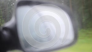 Car side mirror and drivers window with drops of rain sliding down it.