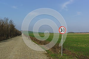 Car sign speed limit 30 kilometers per hour is on the side of the dirt road along the fields of green shoots