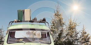 Car with skis and luggage attached to a roof rack in front of snow covered fir trees with shining sun