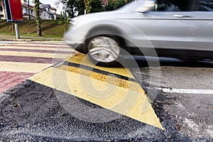 Car slowing down at speed bump or road hump painted in yellow and black stripe. Motion blur intended.