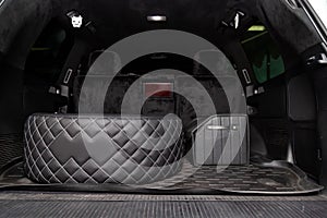 Car spare wheel sheathed in a black leather case and diamond-shaped stitching with white thread in the trunk of an SUV with a tool