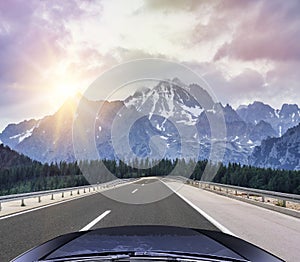 Car speeding on the autobahn among mountain scenery.