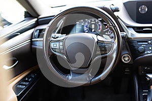 Car steering wheel. Brown leather dashboard, climate control, speedometer, display, wood decoration. Expensive car