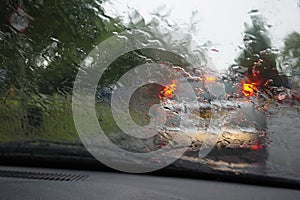 Car tail lights through a rain covered windshield, focus on rain drops