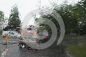 Car tail lights through a rain covered windshield, focus on rain drops
