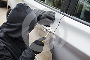 Car thief in action, a man in a hood breaks a screwdriver car door. The man dressed in black trying to break into the car