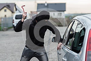 Car thief breaking a glass in car with crowbar