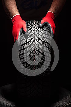 Car tire service and hands of mechanic holding new tyre on black background with copy space for text