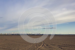 Car tracks in the sandy desert on the background of a modern city with pipes of factories under the blue sky