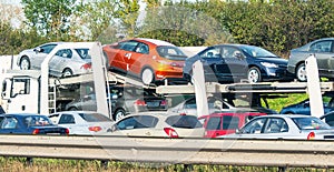 Car trailer transporter laden of new cars among suburban traffic jam