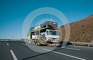 A car transporter carries evacuated cars and a lorry on highway. Long vehicle carrying automobiles.