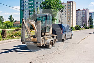 Car is transporting a mini excavator loaded on a trailer