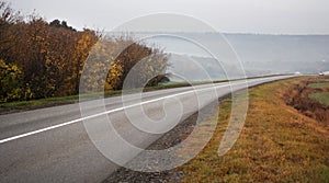 Car traveling on the asphalt road in a rural autumn landscape at sunset