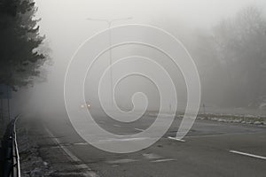 Car traveling on the foggy road with headlights or headlamps on. Low visibility - Dangerous driving of cars in winter in bad