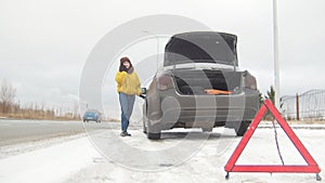 Car trouble. An emergency sign. Car trouble on a snowy country road. Winter. A young woman call the rescue service