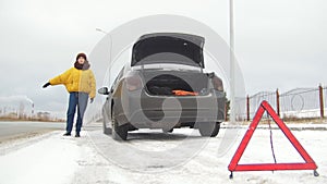 Car trouble. An emergency sign. Car trouble on a snowy country road. A young woman tries to catch the car