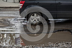 Car tyre about to pass through large pothole full of water
