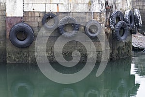 Car tyres hanging on rope against harbour wall at port dock to protect ships and boats