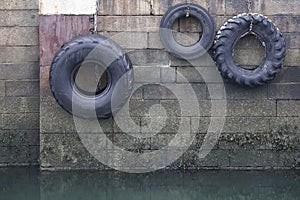 Car tyres hanging on rope against harbour wall at port dock to protect ships and boats