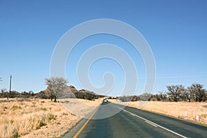 Car view of asphalt road in the desert in perspective with cars driving ahead under a blue sky